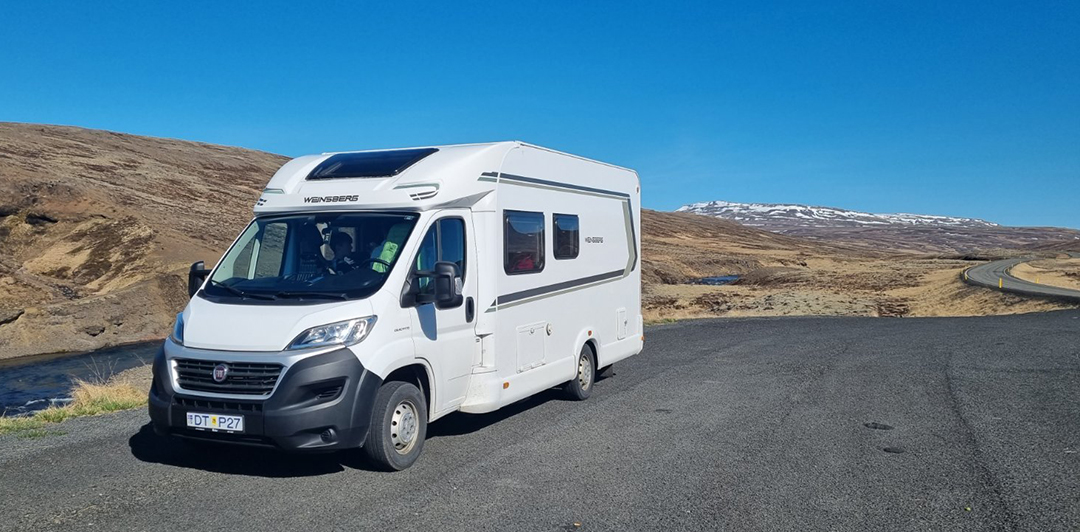 A motorhome on a sunny Icelandic road surrounded by hills and open landscapes, capturing the freedom of travel.