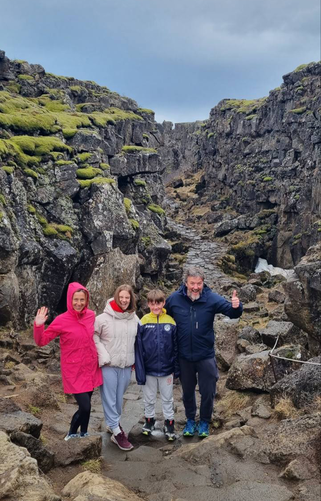 A family standing between two tectonic plates in Þingvellir National Park, surrounded by towering rock walls.