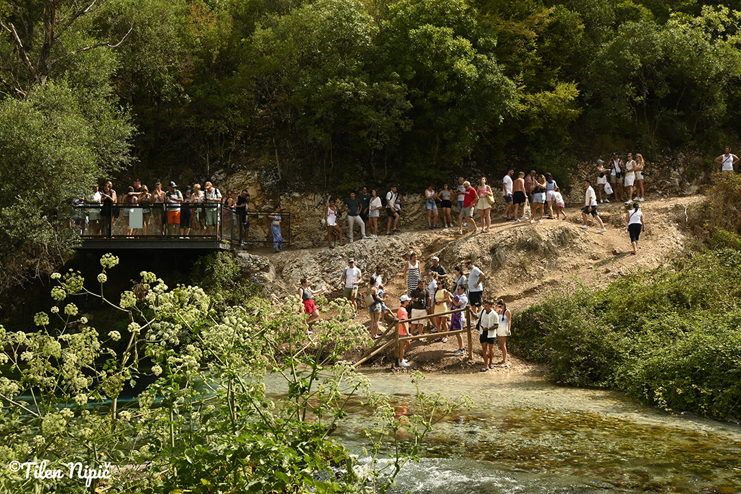 People standing by a river on a scenic viewpoint, surrounded by greenery and rocky landscape in Albania.