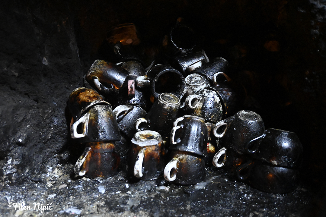 Burnt metal cups stacked in darkness, as a symbol of a difficult past and collective memory in Albania.