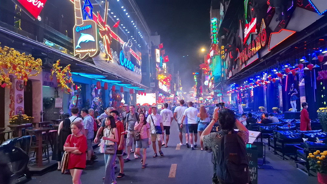 Vibrant Saigon street filled with people, colorful neon lights and the lively pulse of the city's nightlife.