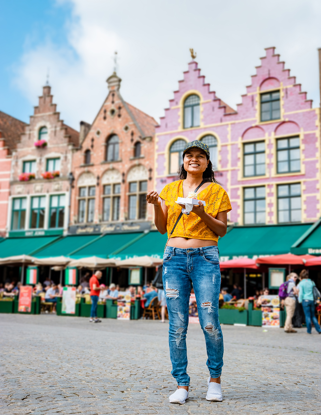 Tourist standing at Markt Square in Bruges with colorful Flemish historic houses in the background.