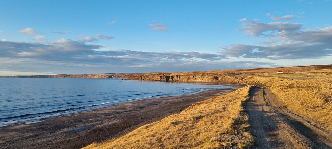 Coast near Husavik in northern Iceland with views of the black sand beach, calm sea and dramatic Icelandic landscape along the North Atlantic.