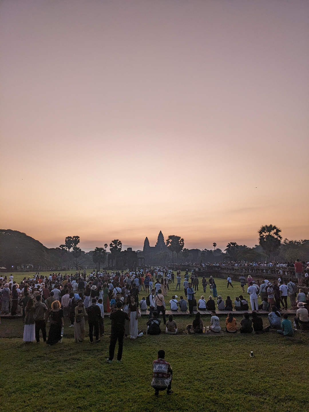 Crowds gathering at sunset in front of Angkor Wat as the sky turns warm evening colors.