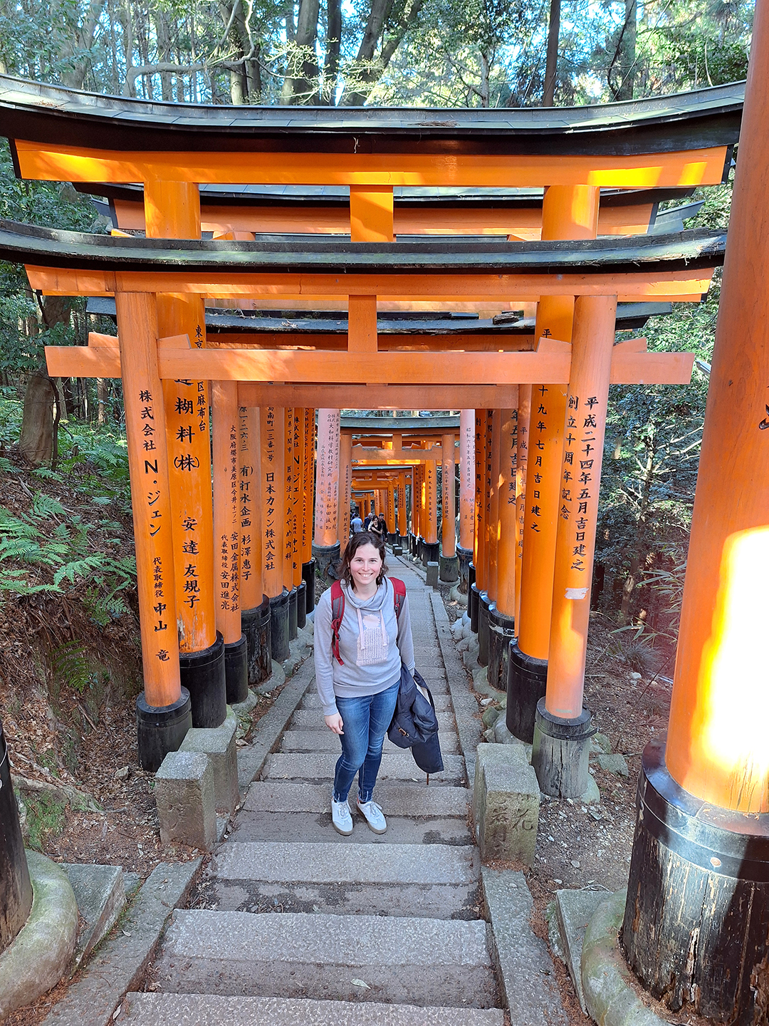 Popotnica med značilnimi oranžnimi vrati torii v svetišču Fushimi Inari v Kyotu, enem najbolj znanih šintoističnih svetišč na Japonskem.