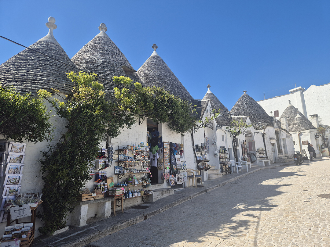 Tradicionalne bele hiške trulli s stožčastimi kamnitimi strehami in trgovinicami v zgodovinskem središču Alberobella v Apuliji.